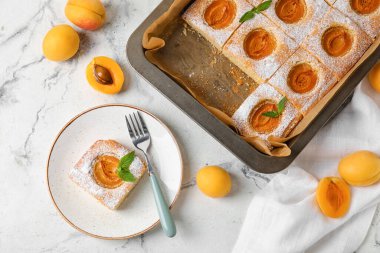 Baking tray and plate with tasty apricot pie on light background