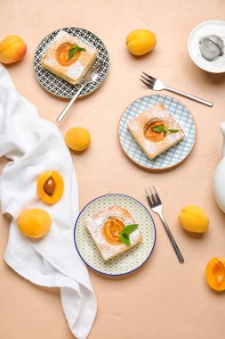 Plates with pieces of tasty apricot pie and fresh fruits on color background