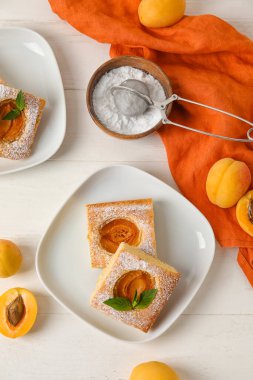 Plates with pieces of tasty apricot pie and sugar powder on light wooden background