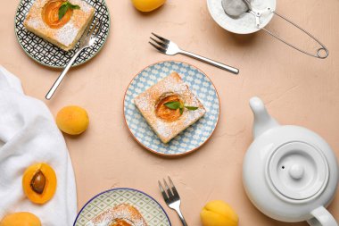 Plates with pieces of tasty apricot pie and teapot on color background