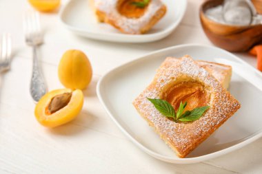 Plate with pieces of tasty apricot pie on light wooden background, closeup