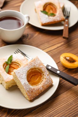 Plate with pieces of tasty apricot pie on wooden table, closeup