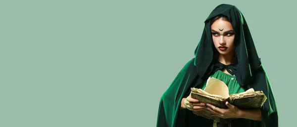 Young witch with spell book on green background with space for text