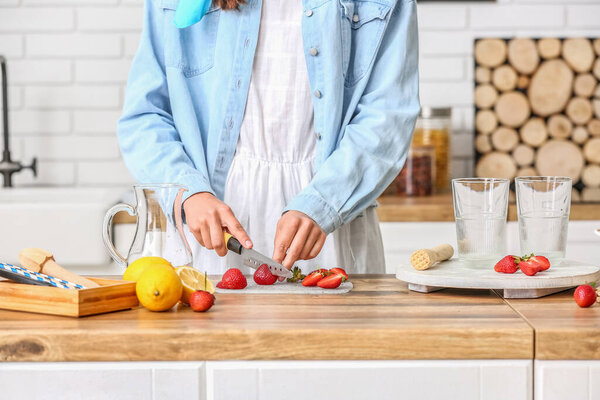 Woman cutting strawberry for tasty lemonade on kitchen counter