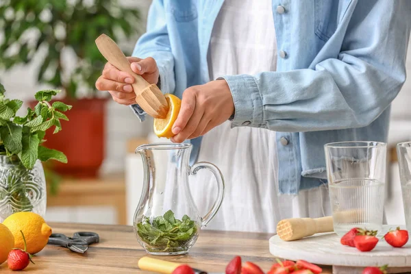 Woman squeezing lemon juice into jug in kitchen