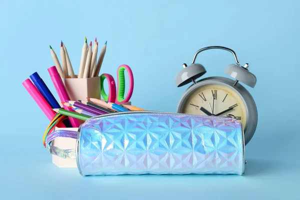 Holographic pencil case with school stationery and alarm clock on blue background
