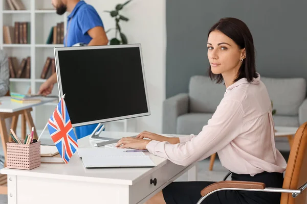 Young English teacher working with computer at table in school