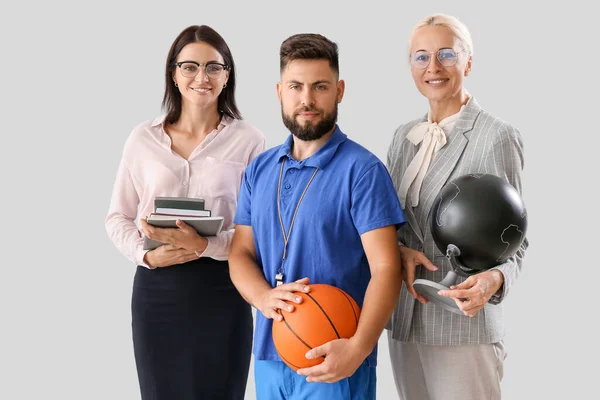 Teachers with ball, books and globe on light background