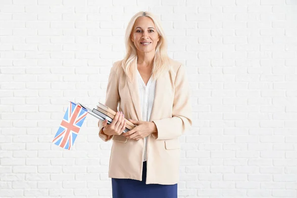 Mature English teacher with UK flag and books on white brick background