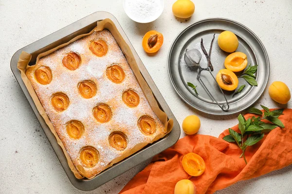 Baking tray with tasty apricot pie and fresh fruits on light table