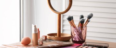 Makeup brushes, cosmetic products and mirror on table in room