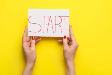 Paper sheet with word START and female hands on yellow background