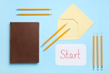Paper sheet with word START, envelope, notebook and pencils on blue background