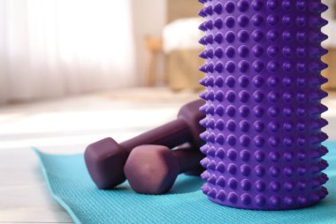 Foam roller and dumbbells on fitness mat in room, closeup