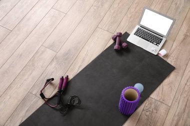 Sports equipment with foam roller, laptop and earphones on wooden floor