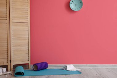 Foam roller and clean towel on fitness mat near pink wall