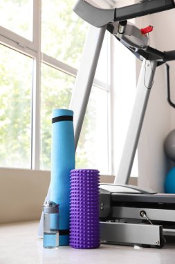 Foam roller with bottle of water and mat near treadmill in gym