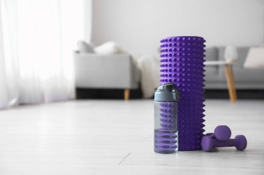 Foam roller with bottle of water and dumbbells in living room