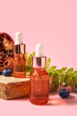 Bottles of essential oil and pomegranate on pink background