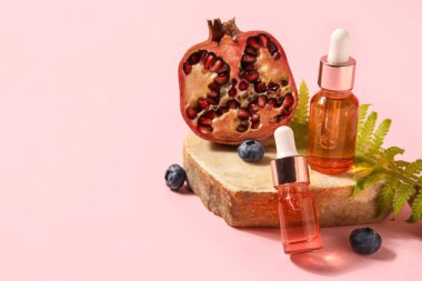 Composition with bottles of essential oil, blueberry and pomegranate on pink background