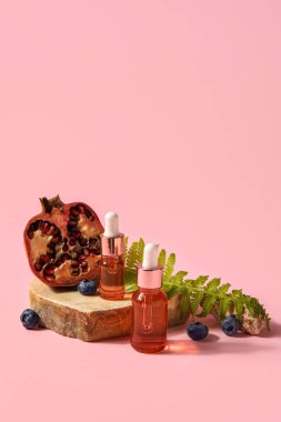 Composition with bottles of essential oil, blueberry and pomegranate on pink background