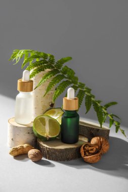 Composition with bottles of essential oil, walnuts, lime and fern leaf on light background