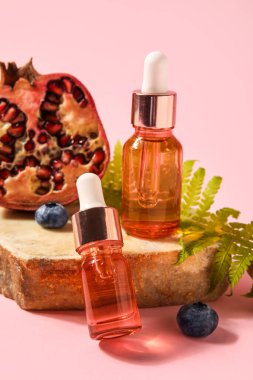 Bottles of essential oil and pomegranate on pink background, closeup