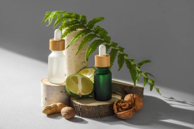 Composition with bottles of essential oil, walnuts, lime and fern leaf on light background