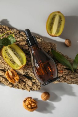 Composition with bottle of essential oil, kiwi, walnuts and tree bark on light background