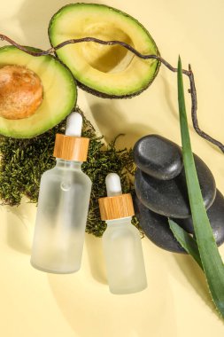 Composition with bottles of essential oil, avocado and spa stones on color background