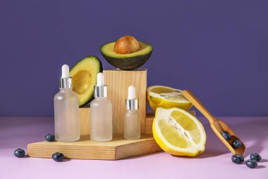 Composition with bottles of essential oil, blueberry, lemon and avocado on color background