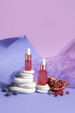 Composition with bottles of essential oil, blueberry, pomegranate and spa stones on color background