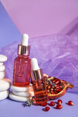 Composition with bottles of essential oil, pomegranate and spa stones on color background