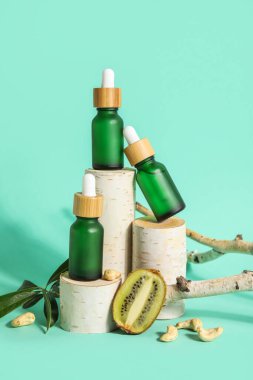 Composition with bottles of essential oil, kiwi and wooden stands on color background