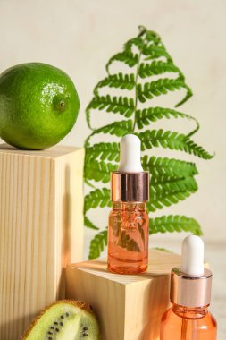 Composition with bottles of essential oil, fern leaf and wooden decor on light background, closeup