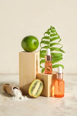 Composition with bottles of essential oil, kiwi, lime and fern leaf on light background