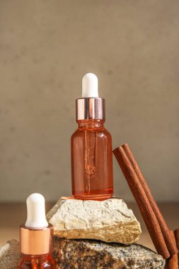 Bottles of essential oil and cinnamon stick on stones against light background, closeup