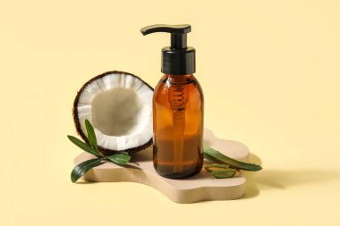 Bottle of natural cosmetic product and coconut on color background