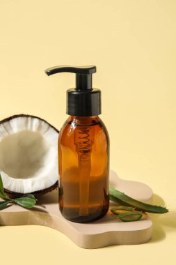 Bottle of natural cosmetic product and coconut on color background
