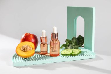 Bottles of essential oil, nectarines and cucumber slices on white background