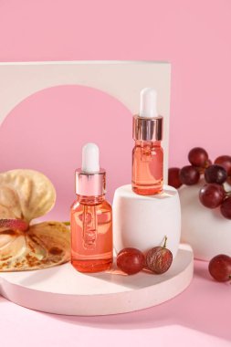 Composition with bottles of essential oil, grapes and plaster decor on pink background
