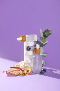 Composition with bottles of essential oil and floral decor on lilac background