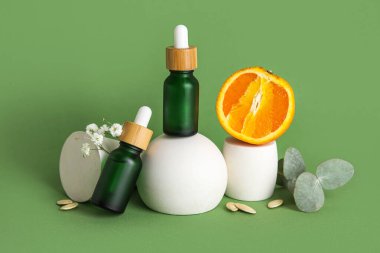 Composition with bottles of essential oil, orange and plaster stands on green background