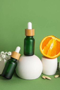 Composition with bottles of essential oil, orange and plaster stands on green background