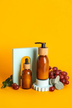 Composition with bottles of natural cosmetic products, grapes and plaster decor on color background