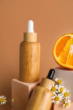 Bottles of essential oil and chamomile flowers on color background, closeup