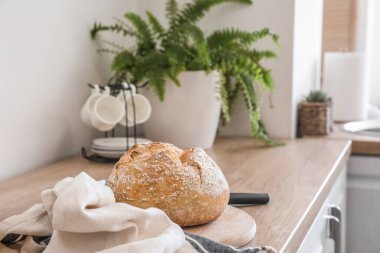 Cutting board with fresh bread and napkin on kitchen counter near light wall