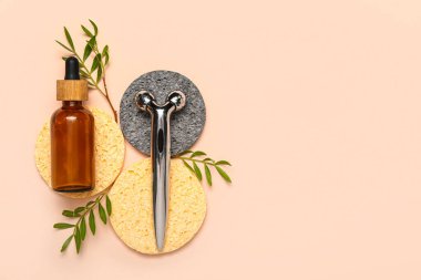 Facial massage tool with cosmetic dropper bottle, sponges and plant branches on beige background