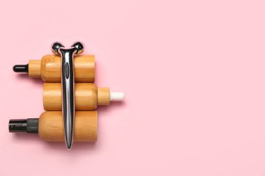 Facial massage tool with cosmetic dropper bottles on pink background