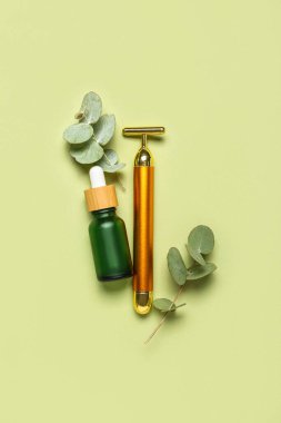 Facial massage tool with cosmetic dropper bottle and eucalyptus branches on green background